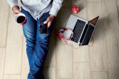 Soft photo of man felling comfort use smartphone on the wooden floor with cup of coffee, headphone, computer laptop and clock, Top view point of copyspace relax time.